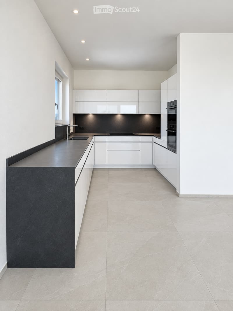 Modern kitchen with white cabinets, black countertops, and a built-in oven. The space features sleek, minimalist design with a large window and recessed lighting.