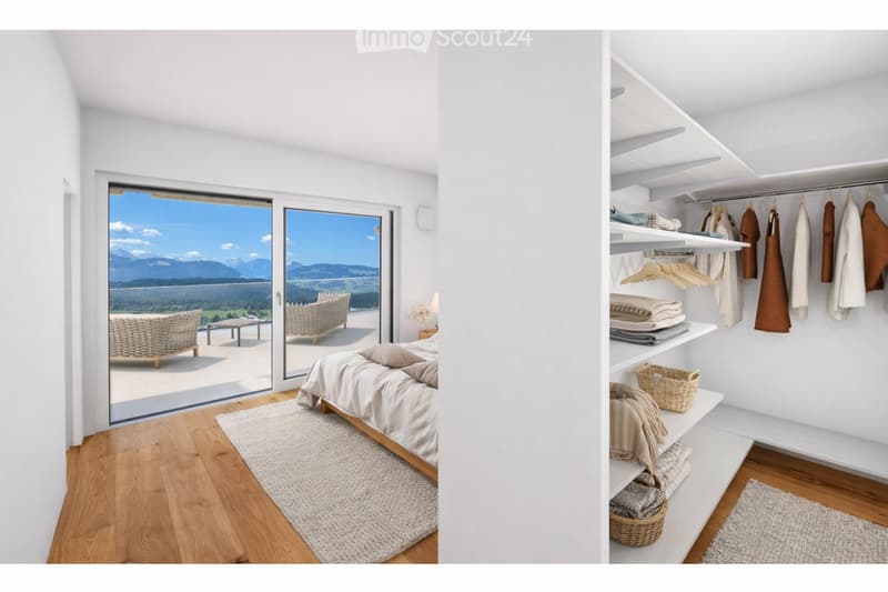 Bright bedroom with wooden flooring, large window offering scenic mountain view, neatly arranged bed with pillows and blanket, built-in wardrobe with shelves and hanging space, and decorative baskets on shelves.