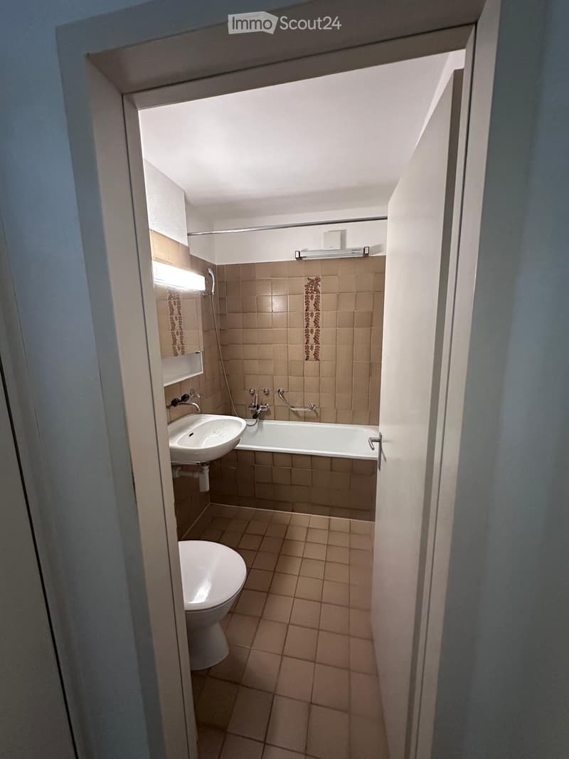 Small bathroom with beige tiles, a toilet, a sink, and a bathtub, viewed from an open doorway.
