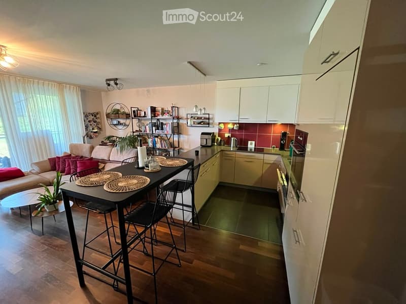 Open-plan living and kitchen area with a sofa, dining table, kitchen cabinets, and appliances.