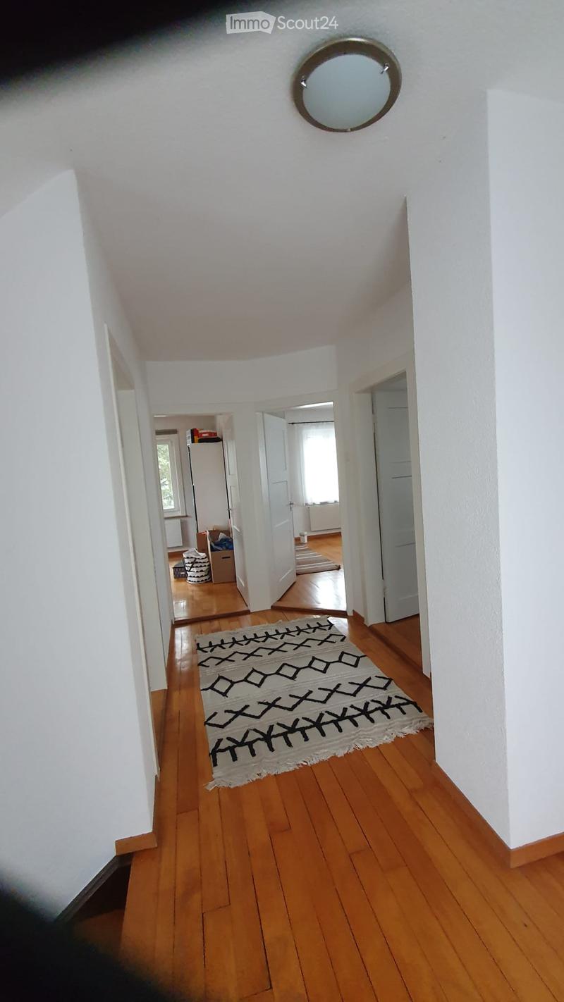 A long, narrow hallway with wooden flooring, white walls, and a round mirror on the ceiling. A patterned rug lies on the floor, and several doors lead to adjacent rooms.
