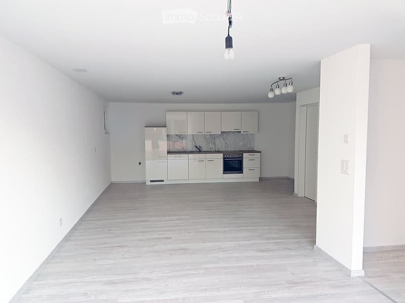 empty room, white walls, wooden floor, open kitchen with built-in appliances