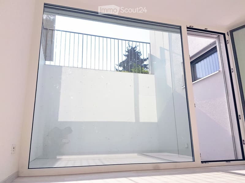 a room with a large glass wall with a balcony and a door