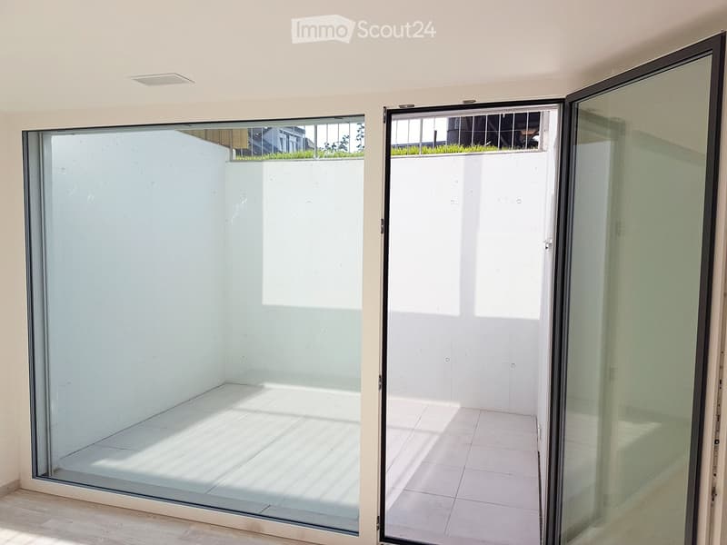 Modern sliding glass doors open to a clean, tiled balcony area with a view of a green lawn and neighboring building.