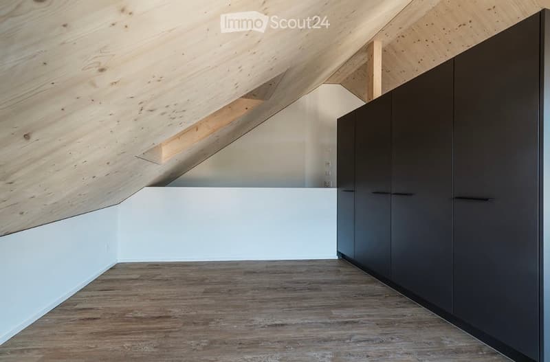 Modern, minimalist attic space with exposed wooden beams, white walls, and dark grey built-in cabinets.