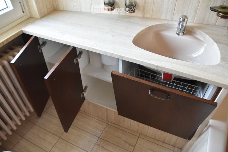 Bathroom with a white countertop sink, chrome faucet, dark wooden cabinets, and a radiator visible on the left side.