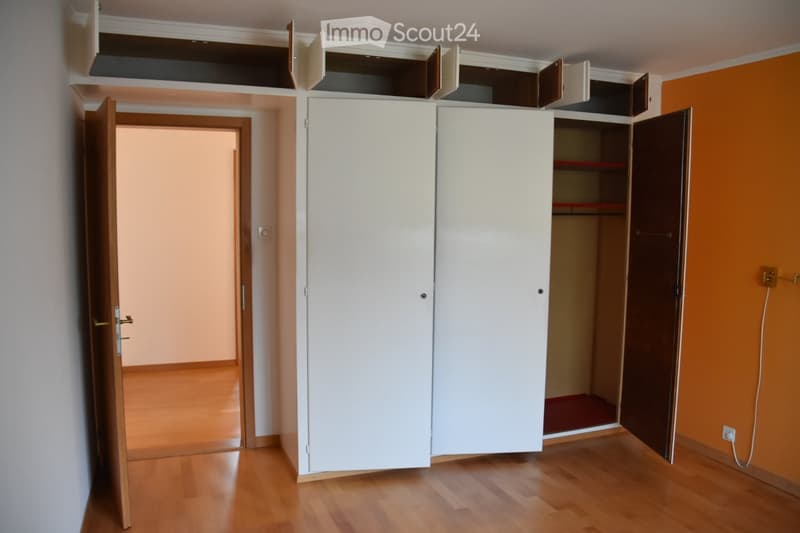 Empty room with wooden flooring, white built-in wardrobes, and an open doorway leading to another room.
