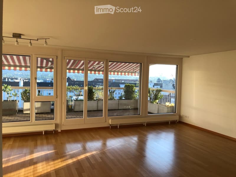 Empty room with wooden flooring, large windows with striped awnings, and radiators along the wall.