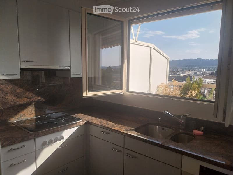 Modern kitchen with granite countertops, white cabinets, electric stove, and a double sink, with large windows offering a city view.