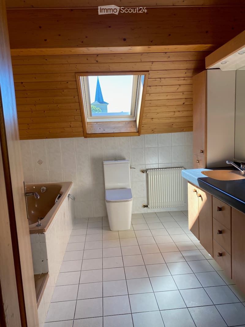 Bathroom with white tiled floor and walls, a toilet, a bathtub, a sink with a cabinet, and a radiator. A skylight window offers a view of a church spire.