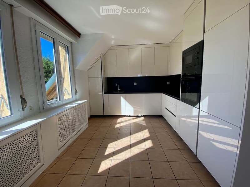 Modern kitchen with white cabinets, tiled floor, and large windows allowing natural light. Features a microwave and oven.