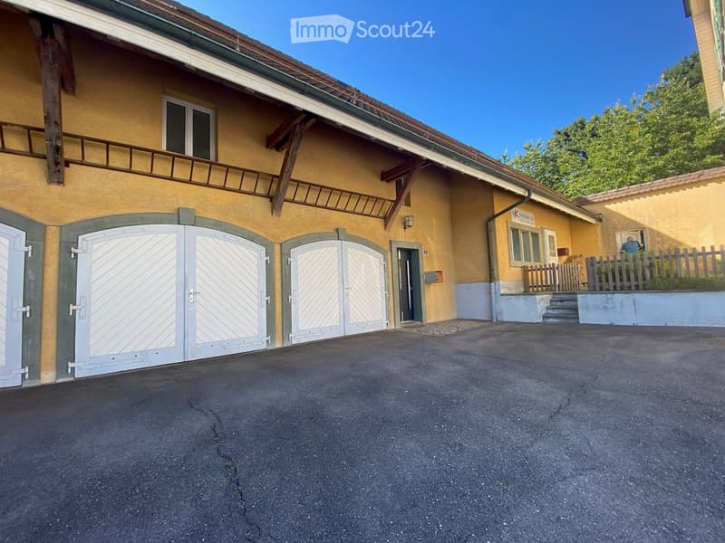 Two-story yellow building with large garage doors, a balcony, and a small garden area with a wooden fence.