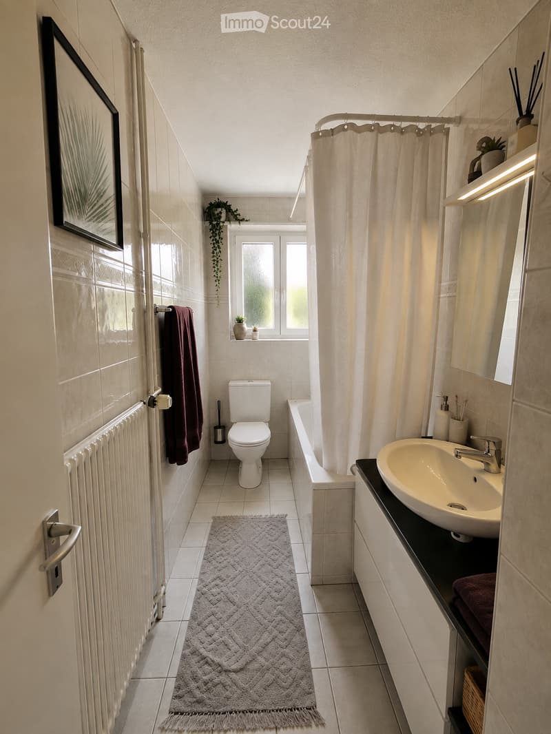 Modern bathroom with white tiles, a toilet, a sink with a mirror, a bathtub with a curtain, a towel, a small plant, and a picture frame on the wall.