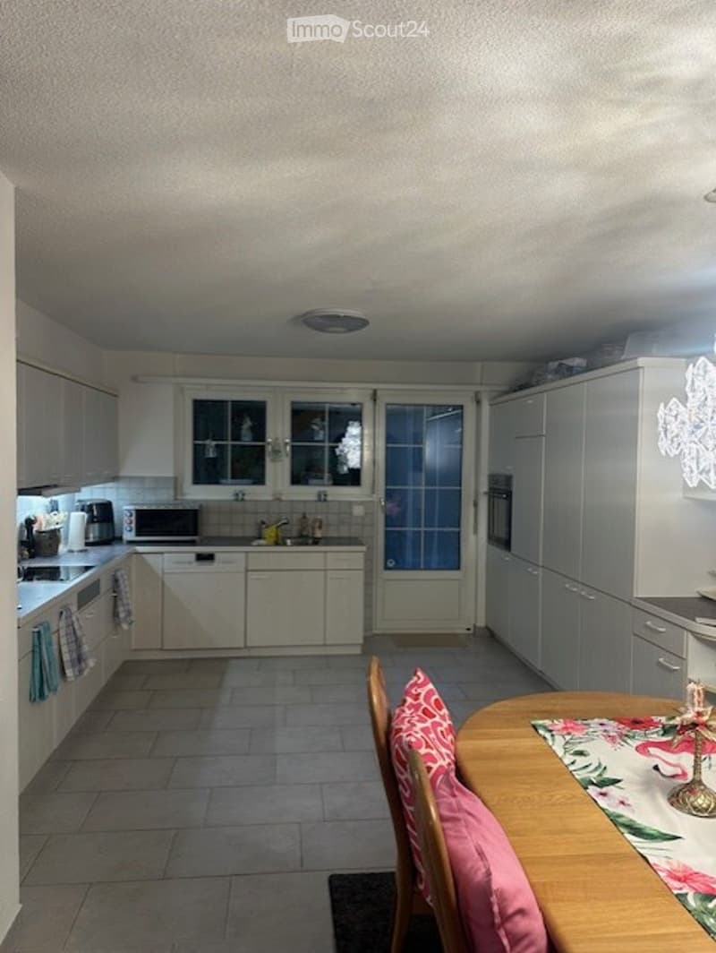 Bright kitchen with white cabinets, a microwave, oven, dishwasher, and a small dining area with a wooden table and chairs.