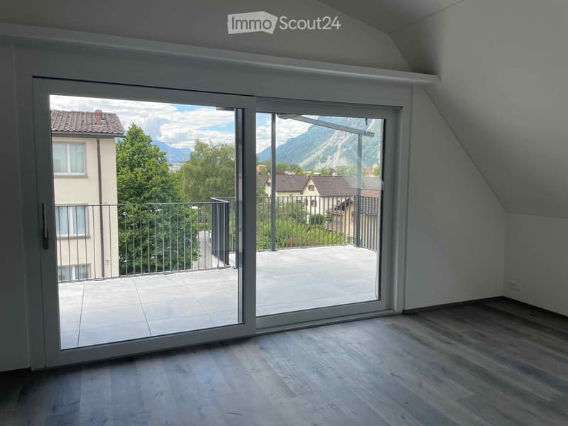 Empty room with wooden flooring and large sliding glass doors leading to a balcony with a scenic mountain view.