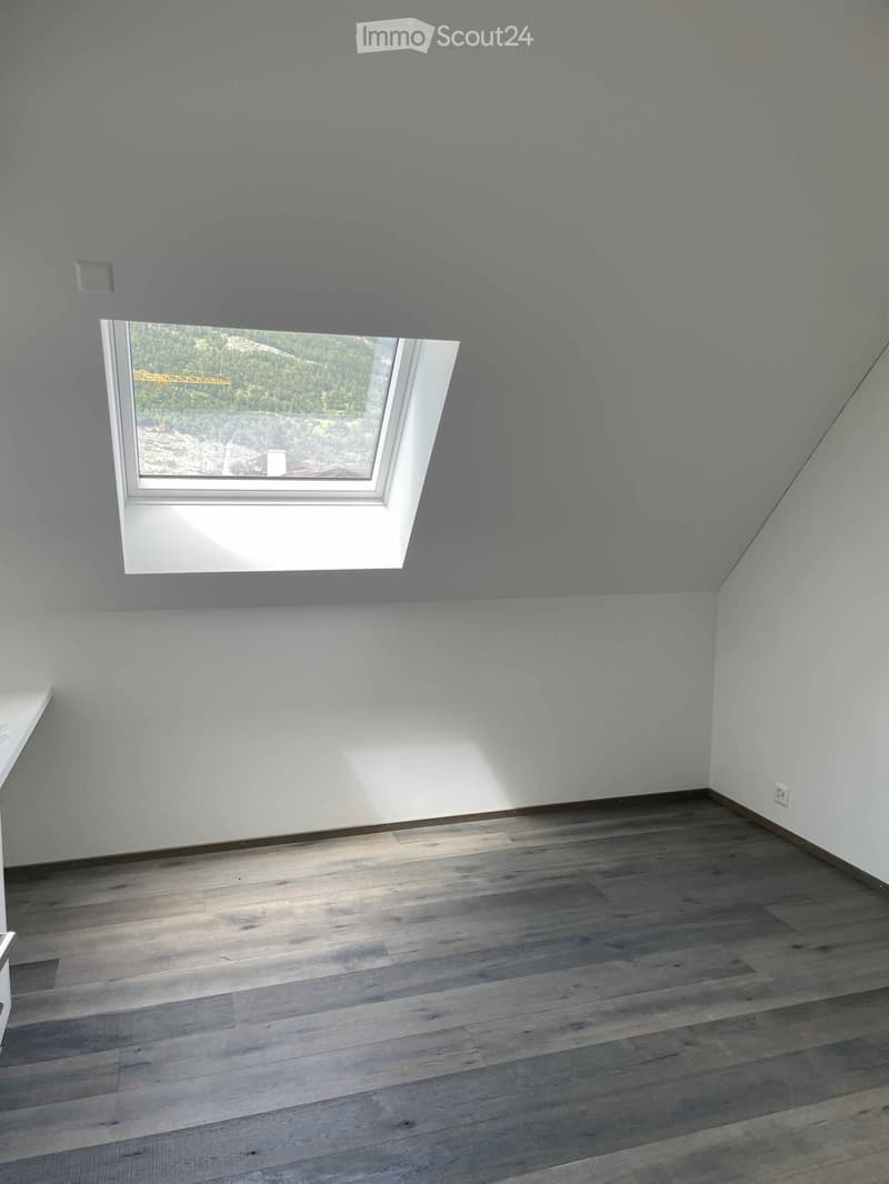 Empty room with light blue walls, wooden flooring, and a skylight window showing a view of the outdoors.