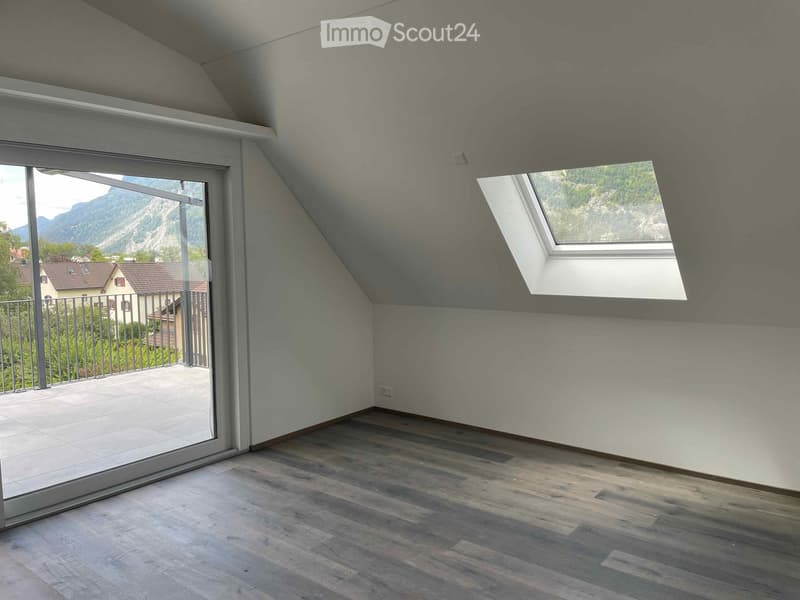 Empty attic room with wooden flooring, large skylight window, and sliding glass door leading to a balcony with a scenic mountain view.