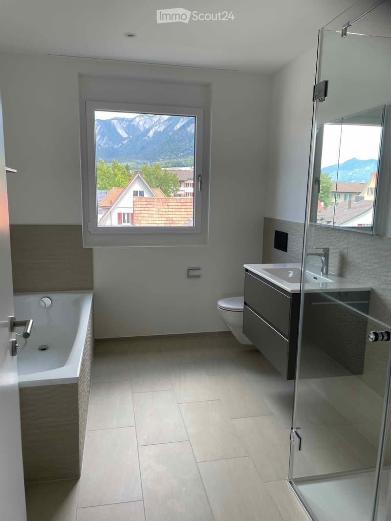 Modern bathroom with a bathtub, toilet, sink, and large window offering a scenic mountain view.