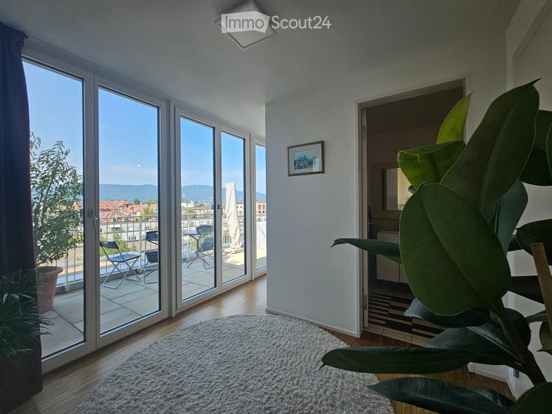 Bright living room with large sliding glass doors leading to a balcony, featuring a white shag rug, a picture frame on the wall, and a view of the city and mountains.