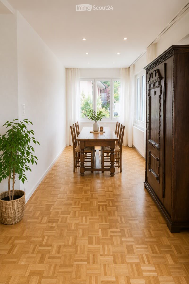 Bright dining room with wooden herringbone flooring, large windows with white curtains, a wooden dining table with six chairs, a tall wooden cabinet, a potted plant, and a vase with a candle on the table.