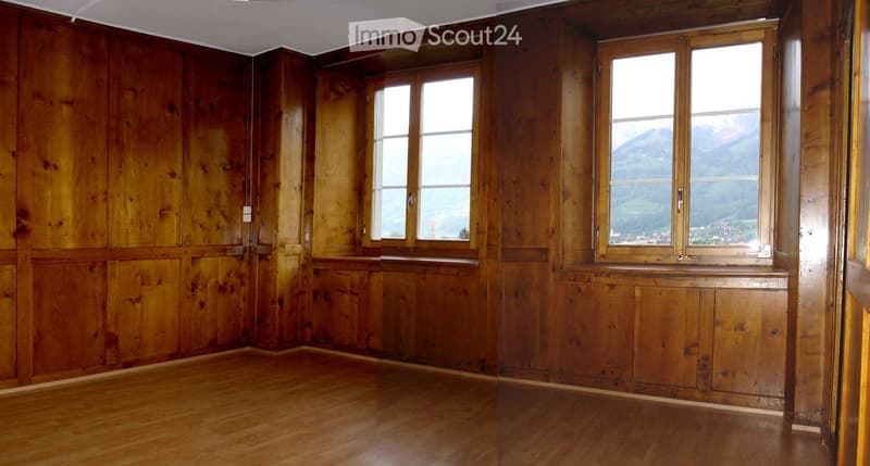 Empty room with wooden walls and floor, large windows offering a scenic mountain view.
