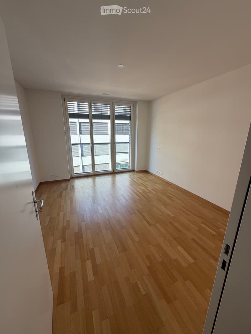 Empty room with light wooden flooring, white walls, and large glass sliding doors leading to a balcony.