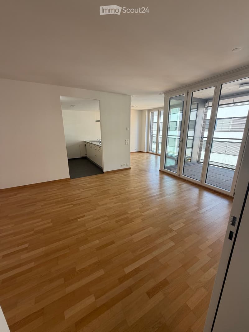 Empty room with light wooden flooring, white walls, and large sliding glass doors leading to a balcony area. The room is unfurnished and has a clean, minimalist design.