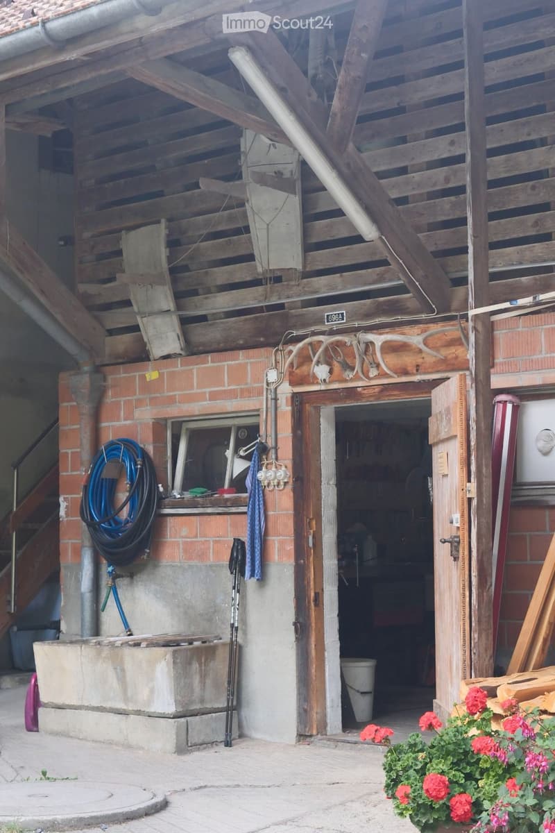 Wooden and brick building with a covered entrance, tools, and outdoor equipment visible.