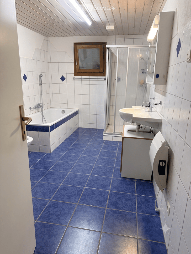 Bathroom with blue tiled floor, white tiled walls, bathtub, double sink, mirror, and shower stall.