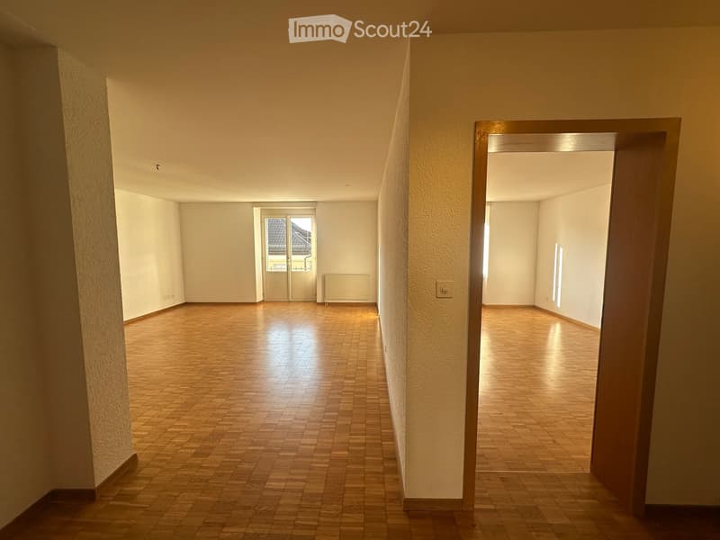 Empty hallway with wooden flooring, white walls, and a door leading to another room.