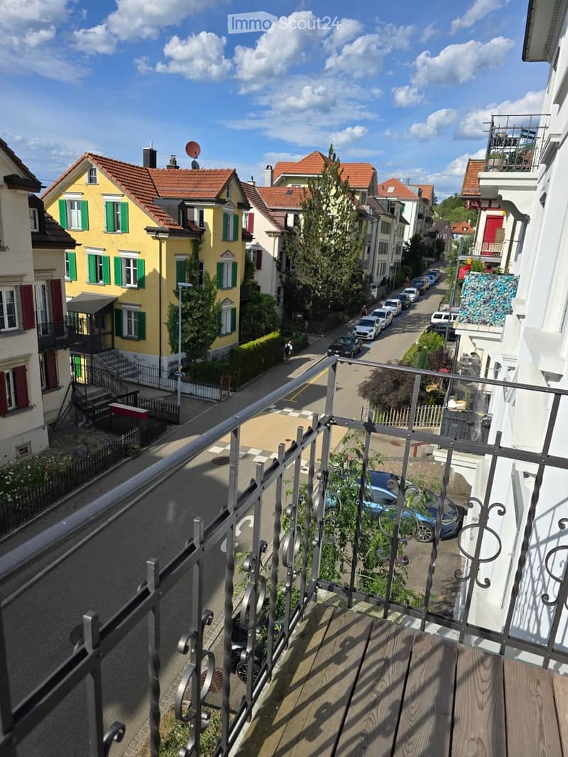 Balcony overlooking a residential street with colorful houses, parked cars, and greenery.