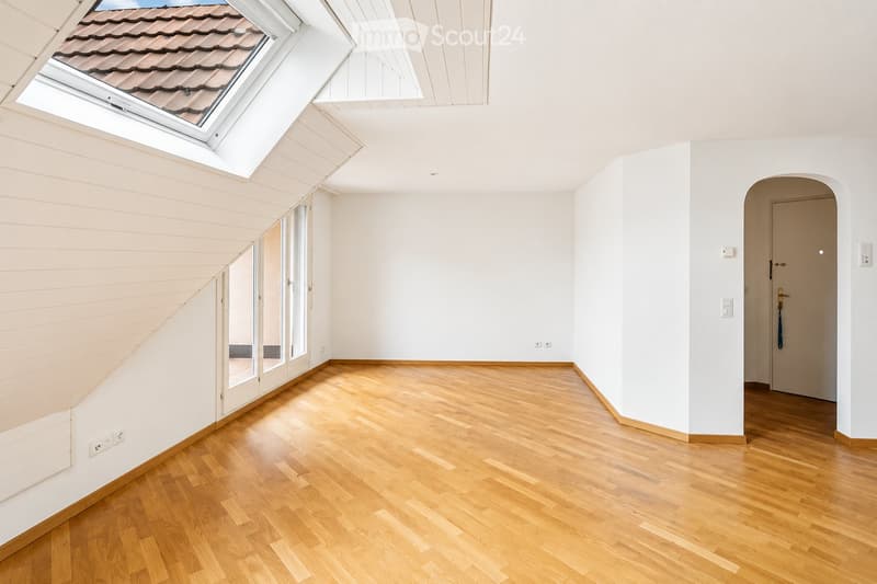 Bright, empty room with wooden flooring, white walls, large skylight, and a door leading to another space.