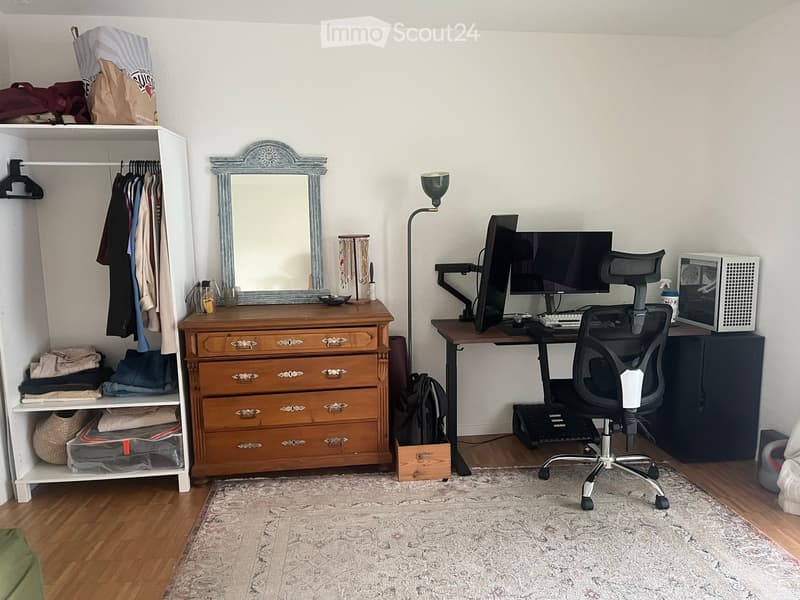 A well-organized bedroom with a wooden dresser, a desk with a laptop, a chair, a mirror, and a closet with clothes and storage items.
