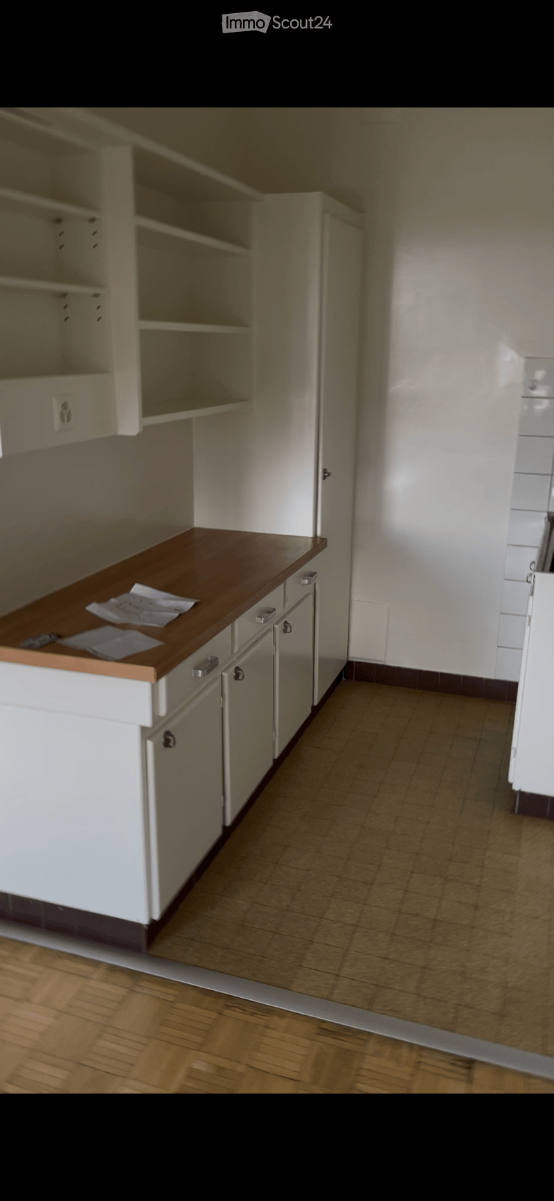 Empty kitchen with white cabinets, wooden countertop, and tiled floor. No appliances or furniture present.