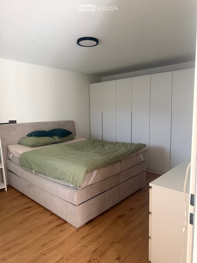 A modern bedroom with a large bed, green bedding, a built-in wardrobe, and a nightstand.