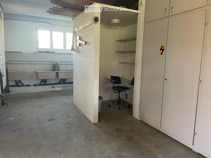 Empty room with concrete floor, white tiled wall, built-in sink area, and a small office area with a chair and shelves.