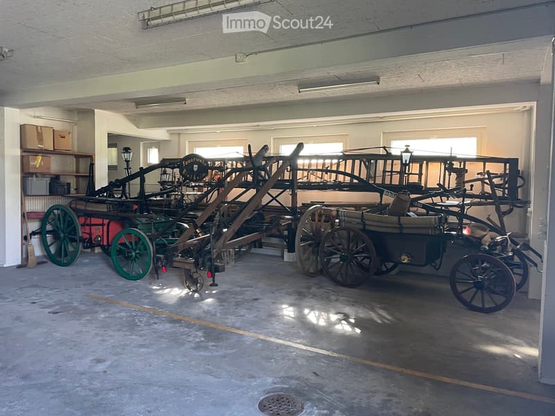 Garage with two vintage fire engines and carriages, exposed ceiling beams, and storage shelves.