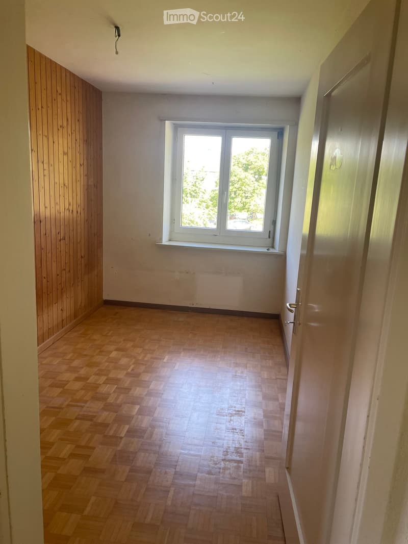 Empty hallway with wooden flooring, white walls, and a large window at the end, allowing natural light to enter.