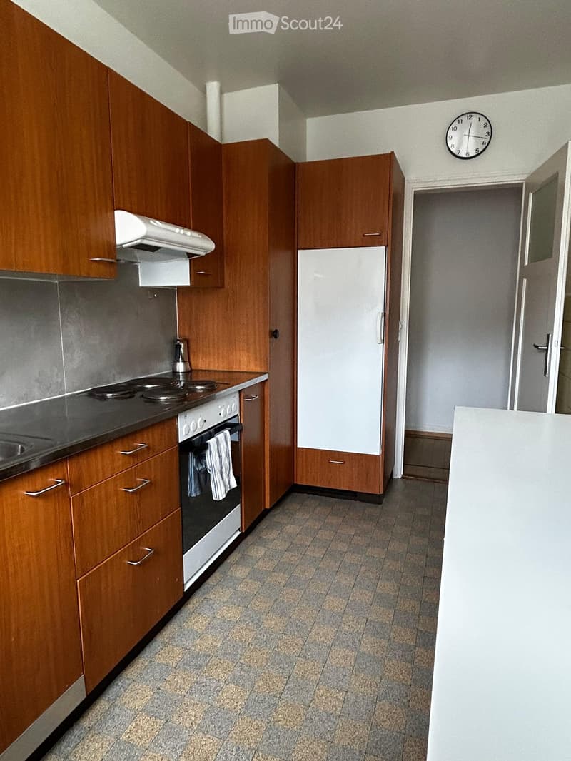 Kitchen with wooden cabinets, a refrigerator, an oven, a stove, a sink, and a clock on the wall.