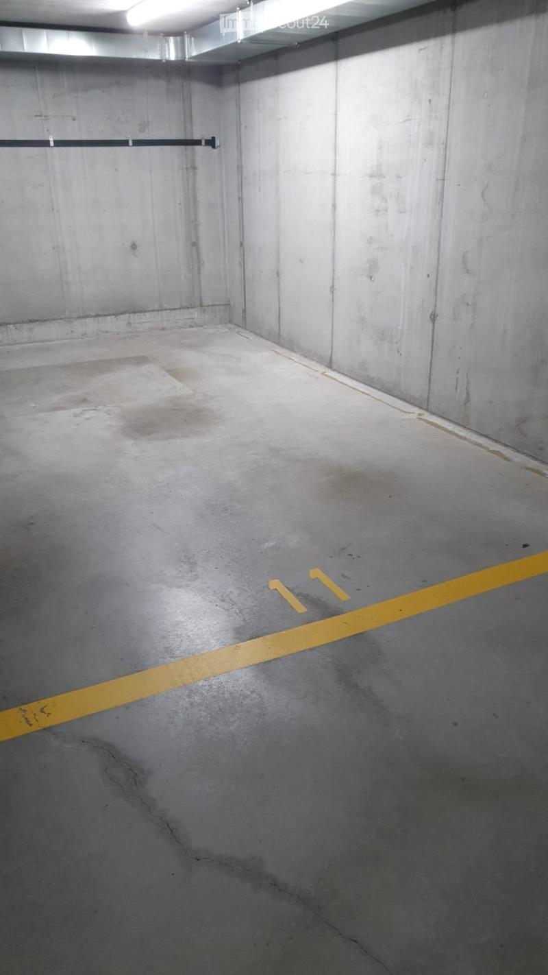 Empty underground parking space with concrete walls and floor, marked with yellow lines and numbers for parking spots.