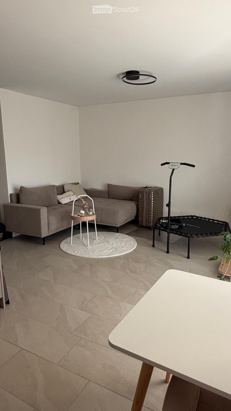 Living room with a grey sofa, small round table, white coffee table, suitcase, mini trampoline, and a potted plant.