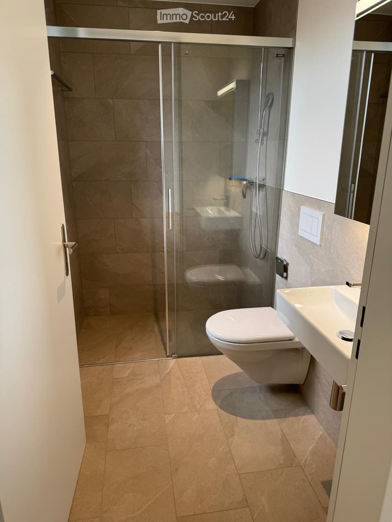 Modern bathroom with beige tiles, a toilet, a sink, and a glass-enclosed shower stall.