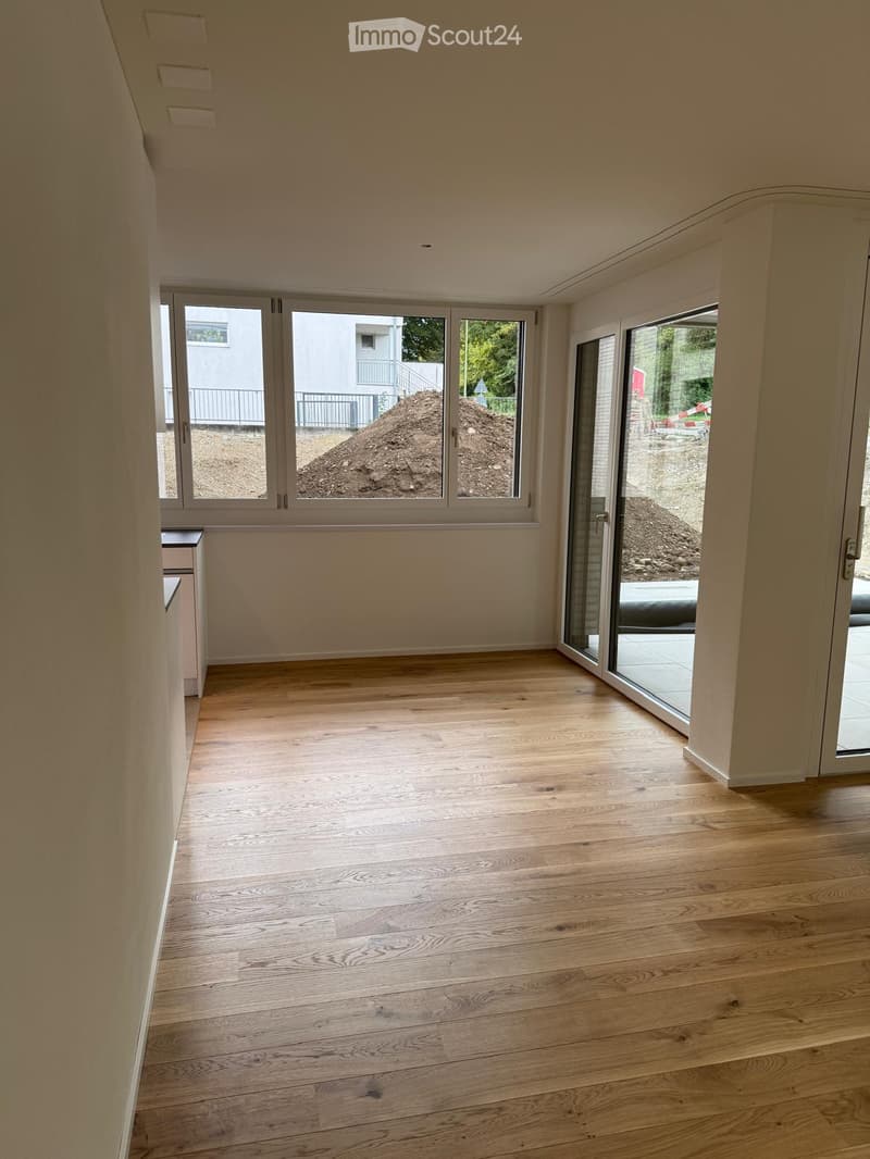 Empty room with light wooden flooring, large windows, and sliding glass doors leading to an outdoor area.