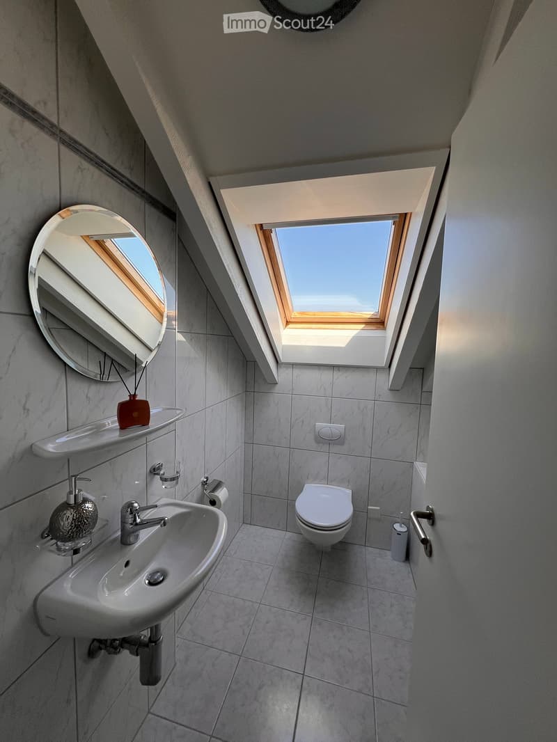 Modern bathroom with a sink, toilet, mirror, and skylight window. Features marble tiles and sleek fixtures.