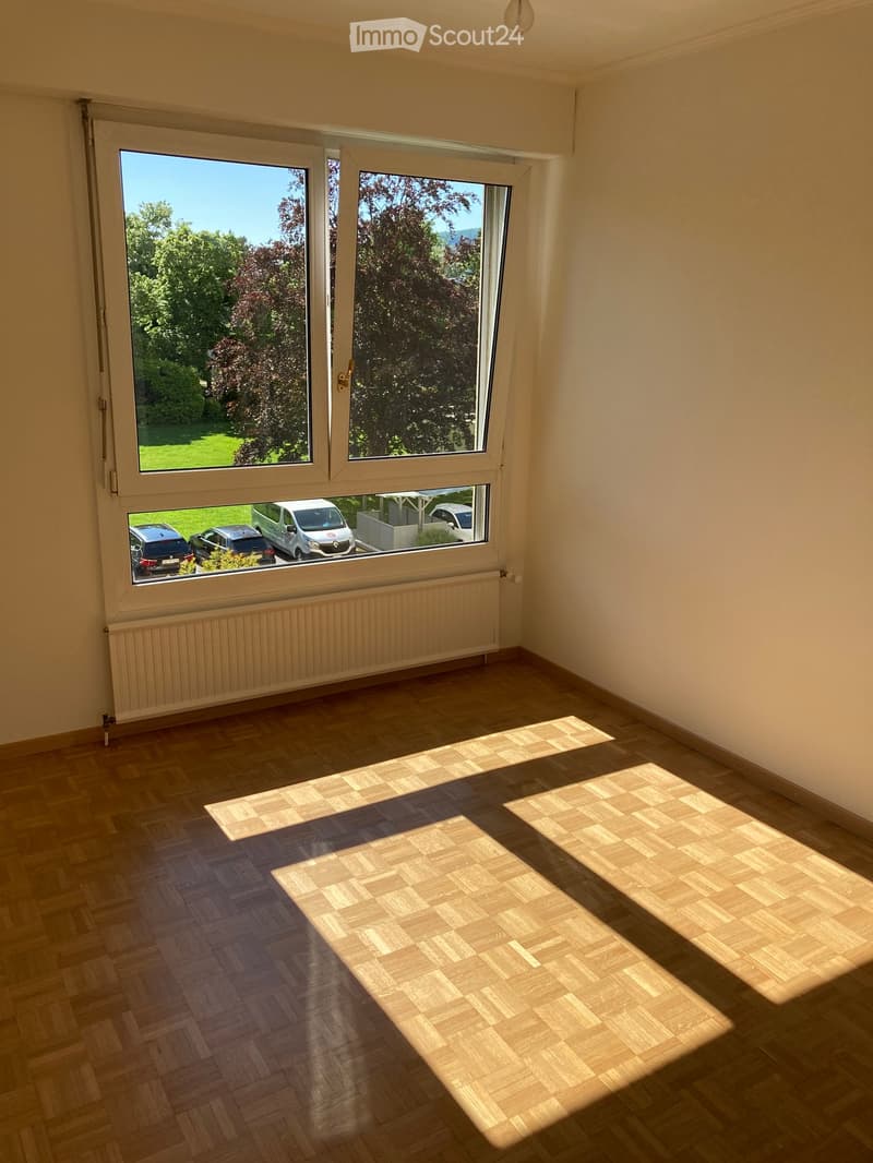 Empty room with wooden flooring, large windows, and a radiator. Natural light streams in from the windows, casting shadows on the floor.