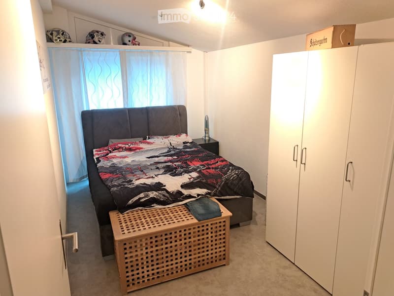 Bedroom with a double bed, nightstand, wicker basket, and a large wardrobe. The bed has a colorful quilt and pillows, and there are helmets on top of a cabinet.