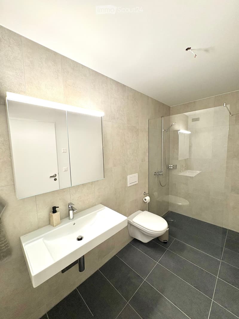 Modern bathroom with a white sink, chrome faucet, toilet, large mirror with built-in lighting, and a glass-enclosed shower area.