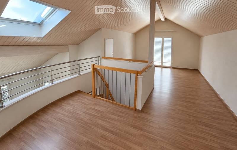 Spacious hallway with wooden flooring, modern metal railing, and skylight above. The walls are painted in a light neutral color, and the ceiling has a wooden finish.