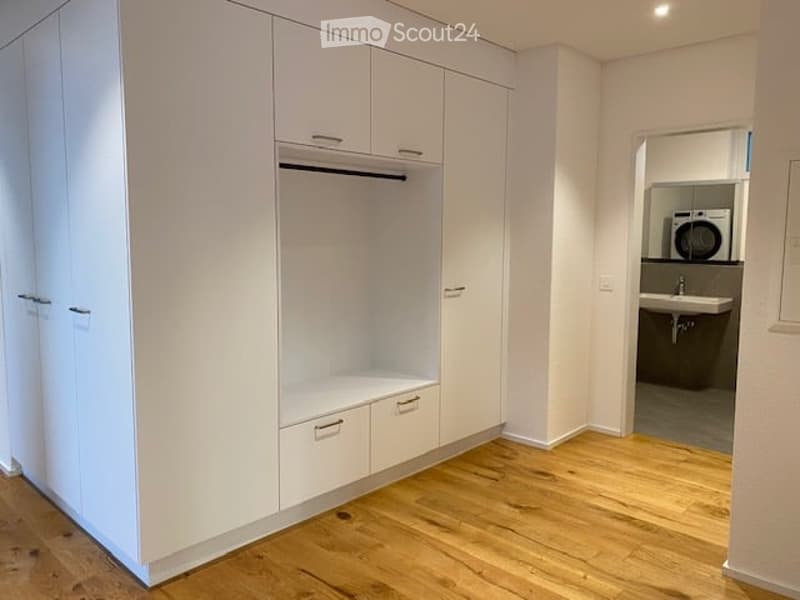 Empty room with white built-in closet and wooden flooring, adjacent to a small bathroom with a washing machine.