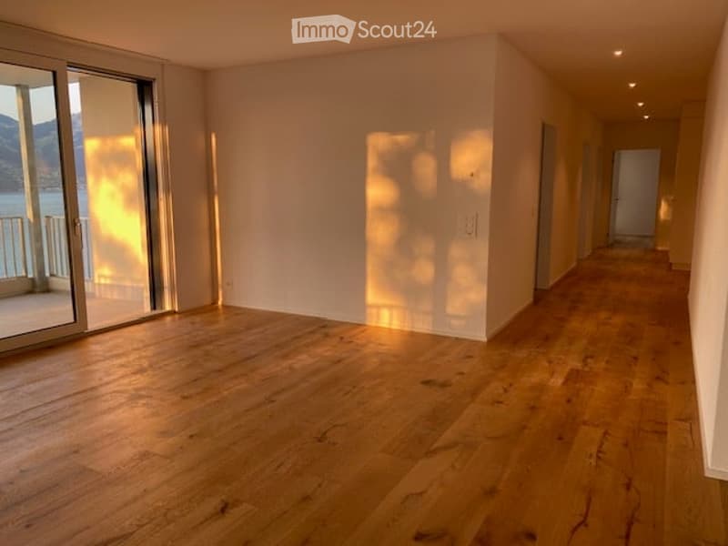 Empty room with wooden flooring, large sliding glass door leading to a balcony with a scenic view, and bright natural light.